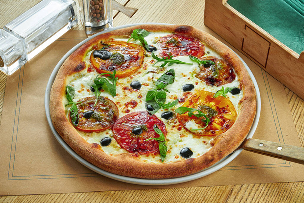 Appetizing baked pizza with melted cheese and different types of tomatoes with a crispy crust on a wooden background. Restaurant serving. Pizza Margherita - Foto, imagen