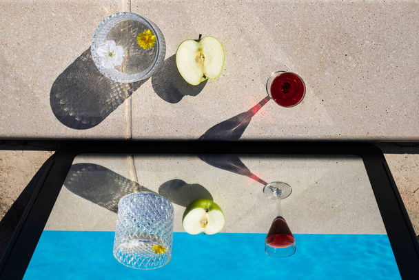twee glazen en een appel naast het zwembad met het spiegeleffect - Foto, afbeelding