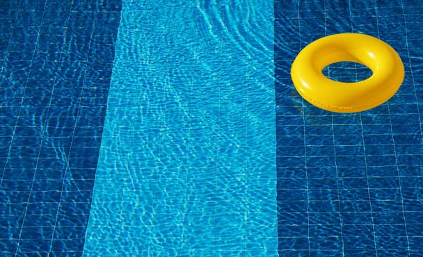 Flotteur de piscine jaune, anneau flottant dans une piscine bleue rafraîchissante - Photo, image