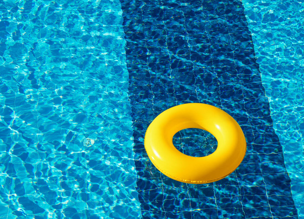 Flotador amarillo de la piscina, anillo flotando en una refrescante piscina azul - Foto, imagen
