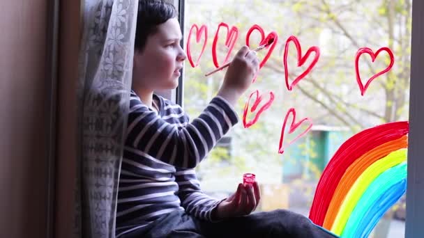 Elszigeteltség. A fiú vörös szíveket rajzol az ablakra. Karantén. Öröm. Szivárvány - Felvétel, videó