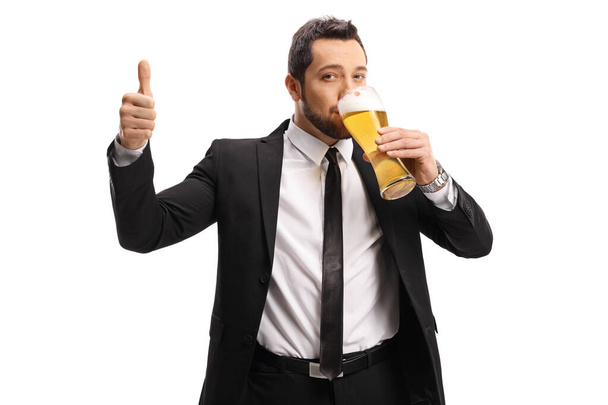 Young man in a suit and tie drinking beer and showing thumbs up isolated on white background - Fotoğraf, Görsel