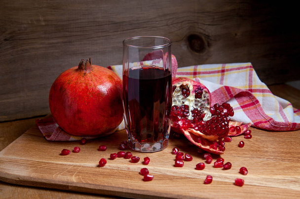 Склад стиглого червоного граната і склянки свіжого рум'яного соку на дерев'яному фоні. крупним планом вид на насіння рубіну гранат фрукти і солодкий свіжий сік в склянці
 - Фото, зображення