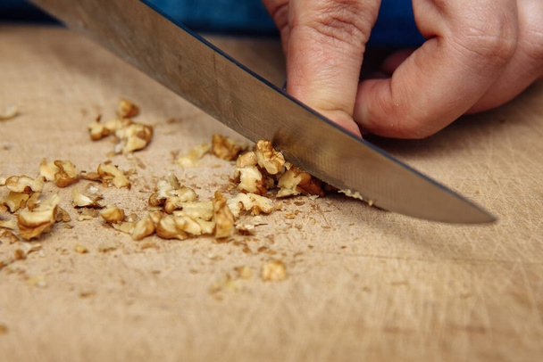Grind, chop walnuts with a knife. Walnuts, kitchen knife, female hands - Foto, afbeelding