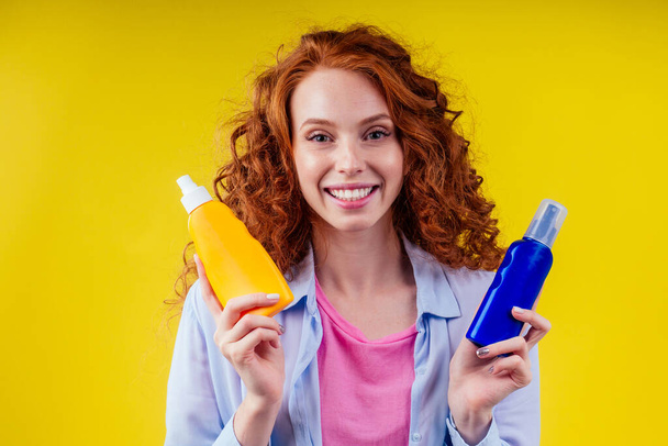 redhaired ginger curly woman holding sunscreen bottle making the right choice in studio yellow background - Foto, afbeelding
