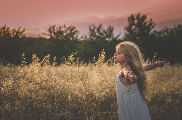 восхитительный маленький ребенок с длинными волосами, отдыхающий в солнечный день на природе в тоне сепии - Фото, изображение