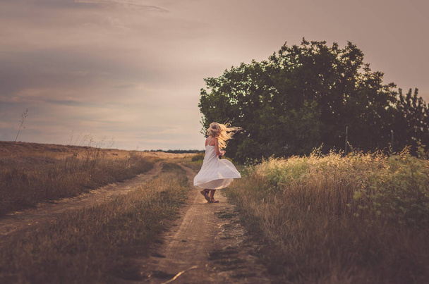 enfant aux longs cheveux blonds soufflant au coucher du soleil dansant gratuitement dans les prairies d'été
 - Photo, image