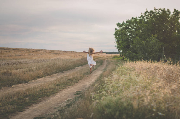niño con el pelo largo y rubio soplando en la puesta del sol bailando gratis en los prados de verano
 - Foto, imagen