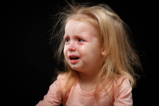 Portrait d'une petite fille blonde en pleurs sur fond noir
 - Photo, image