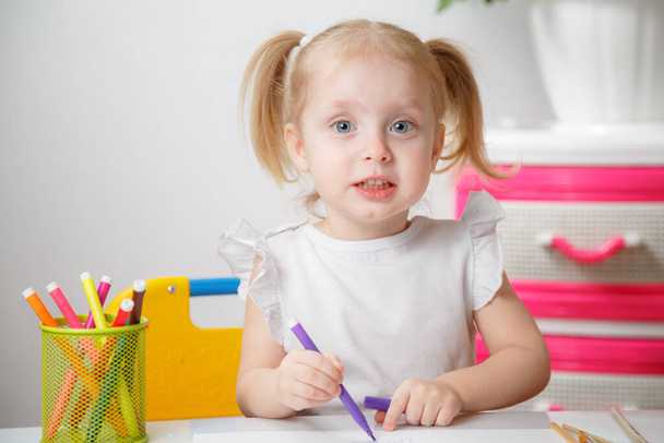 Niedliche kleine 3-jährige Mädchen in weißem Hemd und Pony Tails zeichnen mit Filzstiften zu Hause - Foto, Bild