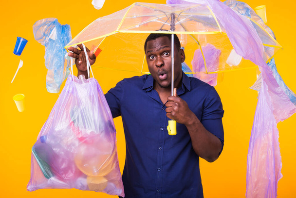 Problem of trash, plastic recycling, pollution and environmental concept - surprised man carrying garbage bag on yellow background - Photo, Image