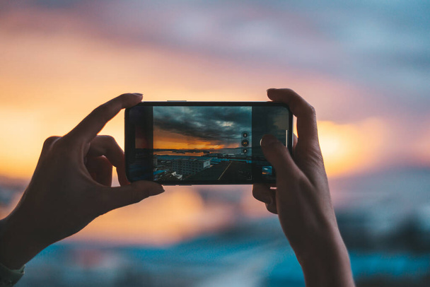 Hände, die ein Smartphone halten und ein Foto des Meeres bei Sonnenuntergang machen - Foto, Bild