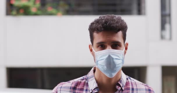 Portrait of a Caucasian man wearing a face mask against coronavirus, covid 19 out and about in the city streets during the day, looking straight into a camera. - Filmmaterial, Video