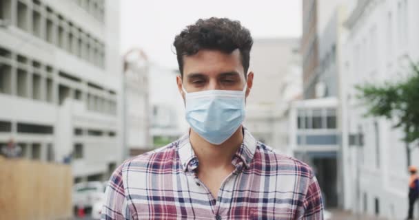 Portrait of a Caucasian man wearing a face mask against coronavirus, covid 19 out and about in the city streets during the day, looking straight into a camera. - Πλάνα, βίντεο