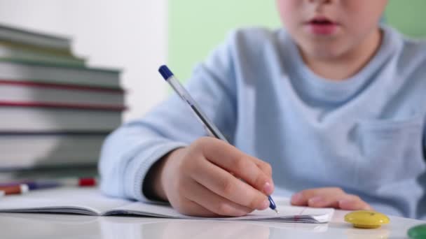 niño pequeño escribe la tarea en un cuaderno, niño varón enseña lecciones en casa sentado en la mesa, primer plano
 - Metraje, vídeo