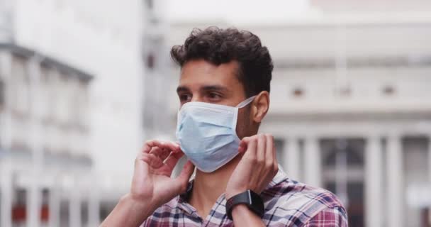 Portrait of a Caucasian man putting on a face mask against coronavirus, covid 19 out and about in the city streets during the day. - Filmagem, Vídeo