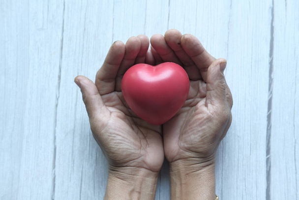 Frau hält rotes Herz in Händen auf Holztisch . - Foto, Bild