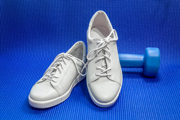 Zapatos deportivos y una mancuerna en una esterilla de yoga. Concepto: ejercicio en el gimnasio o en casa; mantenerse en forma en cuarentena y autoaislamiento
. - Foto, Imagen
