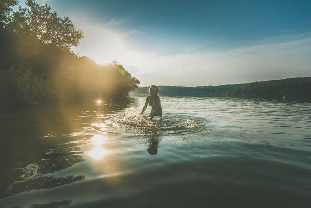 cute girl with long blond hair posing as model in water in golden hour time - Фото, зображення
