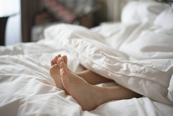 Female feet peeking out from white blanket - 写真・画像