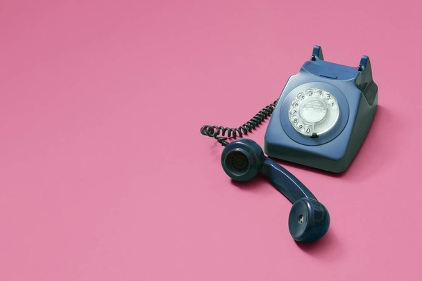 Vintage zabytkowy niebieski telefon obrotowy z podniesionym słuchawką na różowym tle z miejsca do kopiowania i miejsce na tekst z prawej strony składu. - Zdjęcie, obraz