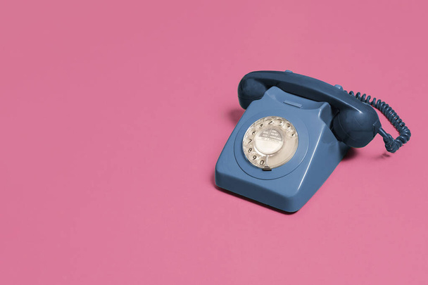 Винтажный антикварный синий вращающийся телефон на розовом фоне с копировальным пространством и местом для текста с правой стороны композиции
. - Фото, изображение