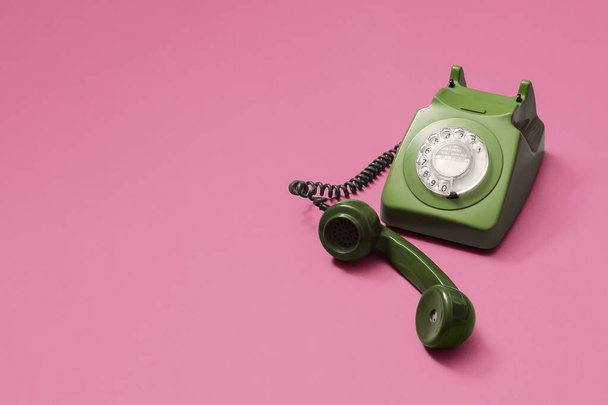 Vintage zabytkowy zielony telefon obrotowy z podniesionym słuchawką na różowym tle z miejsca do kopiowania i miejsce na tekst z prawej strony kompozycji. - Zdjęcie, obraz