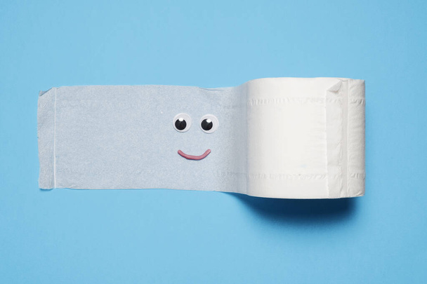 Χαρούμενη και χαμογελαστή πλήρης ρολό χαρτί υγείας ξετυλίγεται σε ένα μπλε backgroud. - Φωτογραφία, εικόνα