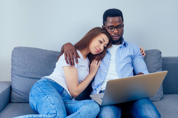 international couple smiling looking at laptop while resting together at home - Photo, Image