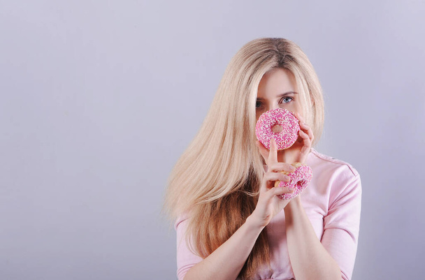  Lächelnde Kaukasierin mit Donuts posiert auf buntem Hintergrund im Studio. - Foto, Bild