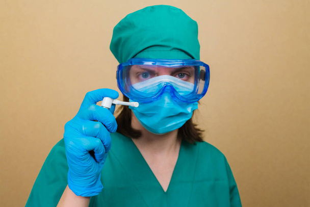 Nainen Lääkäri vihreä puku ja sininen naamio käsineet ja suojalasit antibakteerinen spray kädessään keltaisella pohjalla
. - Valokuva, kuva