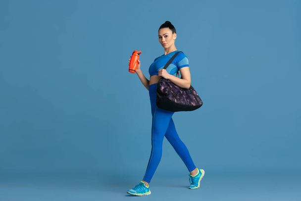 Beautiful young female athlete practicing on blue studio background, monochrome portrait - Fotografie, Obrázek
