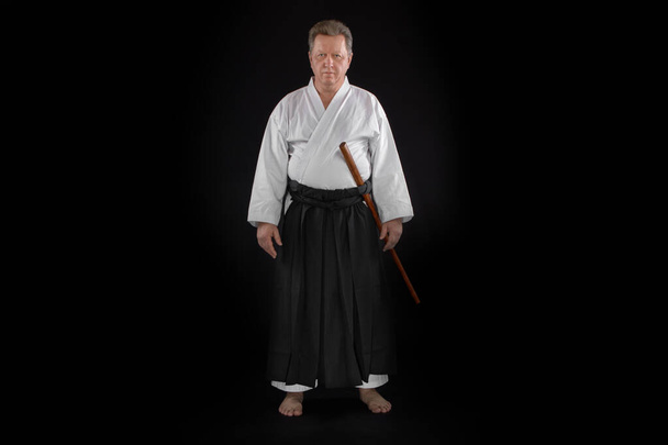 Κοντινό πορτρέτο αϊκίντο master φορώντας παραδοσιακά σαμουράι hakama ρούχα με boken στα χέρια. σε μαύρο φόντο. - Φωτογραφία, εικόνα