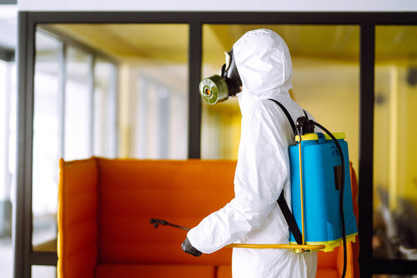 Desinfiointi toimisto estää COVID-19, Mies suojaava hazmat puku spray kemikaaleja leviämisen estämiseksi coronavirus, pandemia karanteenikaupungissa. Puhdistuskäsite
. - Valokuva, kuva