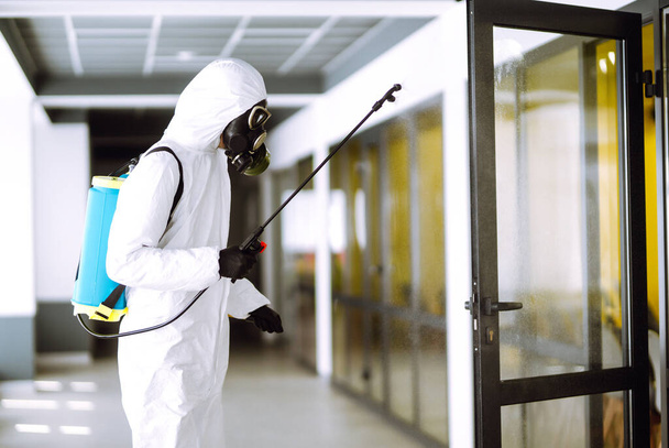 Disinfecting of office to prevent COVID-19, Man in protective hazmat suit with  with spray chemicals to preventing the spread of coronavirus, pandemic in quarantine city. Cleaning concept. - Foto, imagen