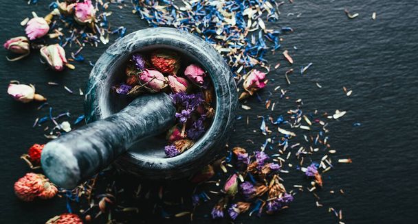 Gyógynövények betakarítása, Ayurveda, alternatív gyógyászat, szárított virágok márvány habarcsban fekete alapon - Fotó, kép