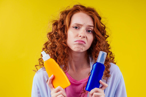 redhaired ginger curly woman holding sunscreen bottle making the right choice in studio yellow background - Fotoğraf, Görsel