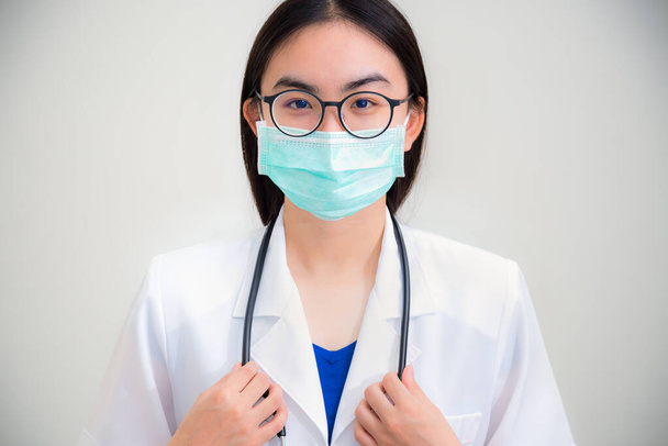 Studio muotokuva edessä kaunis aasialainen nuori nainen lääkäri stetoskooppi valkoinen yhtenäinen kulumista lasit ja vihreä naamio suojella Corona Virus terveyden tarkastellaan kameran harmaa tausta
 - Valokuva, kuva