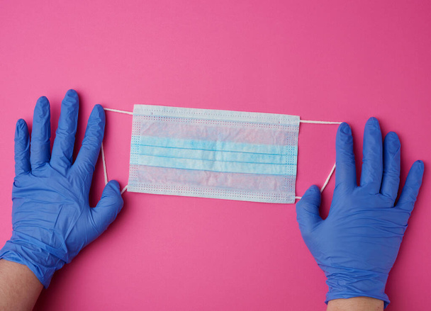 manos sostiene una máscara médica contra virus y bacterias en un fondo rosa, herramienta médica protectora, vista superior
 - Foto, imagen