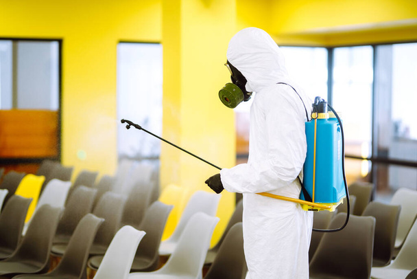 Man wearing protective suit disinfecting assembly hall with spray chemicals to preventing the spread of coronavirus, pandemic in quarantine city. Disinfecting of office. COVID-19. - Фото, изображение