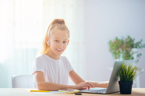 Vakava koulutyttö istuu pöydässä kannettavan tietokoneen ja oppikirjan kanssa ja tekee kotitehtäviä
. - Valokuva, kuva