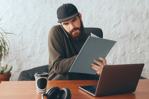 молодий чоловік з бородою робить паперову роботу в офісі за столом
 - Фото, зображення