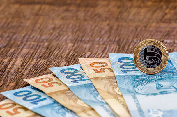 egy valódi érme százötven brazil reais bankjegyen. 100-as és 50-es bankjegy fából készült háttérrel, a pénzügyi válság vagy a brazil gazdaság koncepciójával. - Fotó, kép
