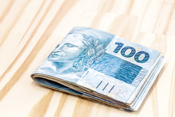 brazil pénz bankjegyek, 100 reais bankjegy, könnyű és rusztikus fából készült háttérrel. Megtakarítás vagy megtakarítás fogalma. - Fotó, kép