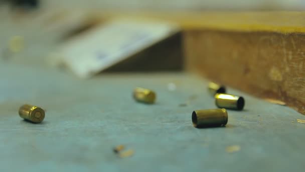 Üres pisztolylövedék lövedékek hullanak le és ütköznek a fa asztalra egy lőtéren. Extrém közeli, szelektív fókusz elmosódott háttérrel és másoló térrel. - Felvétel, videó