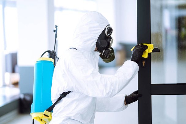 Man in protective hazmat suit washes door handles in office to preventing the spread of coronavirus, pandemic in quarantine city. Cleaning and disinfection of office. Covid-19. - Foto, imagen