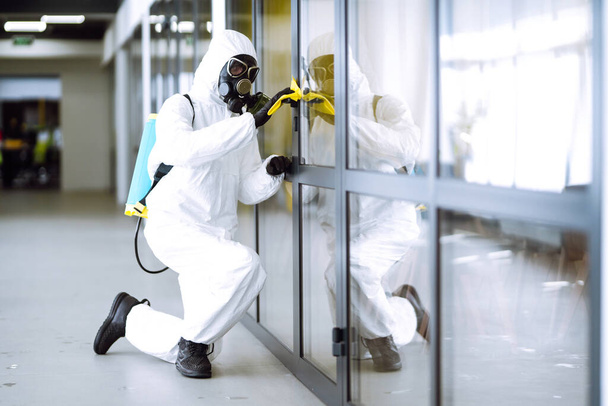 Man in protective hazmat suit washes door handles in office to preventing the spread of coronavirus, pandemic in quarantine city. Cleaning and disinfection of office. Covid-19. - Foto, imagen