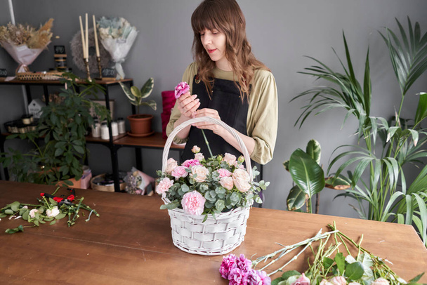 Floral shop concept . Florist woman creates flower arrangement in a wicker basket. Beautiful bouquet of mixed flowers. Handsome fresh bunch. Flowers delivery. - Zdjęcie, obraz