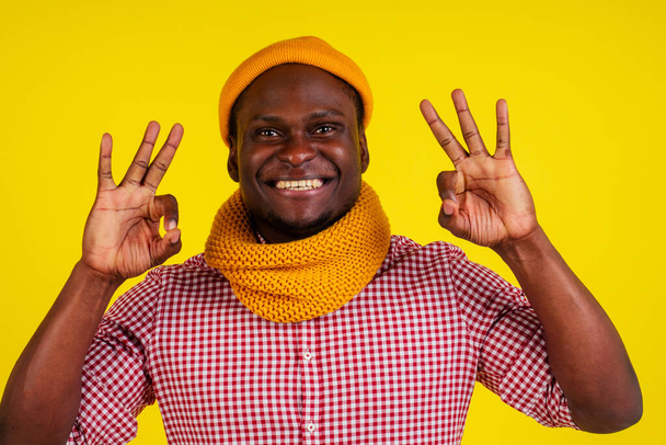 portrait of success attractive african american man in knitted hat and scarf and red checkered shirt excited feeling good-mood.autumn spring fashion look outfit showing okay gesture - Fotografie, Obrázek