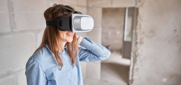 Жінка-архітектор або інженер-будівельник носить окуляри віртуальної реальності всередині будівлі. Бетонні стіни в новій квартирі, концепція ремонту
. - Фото, зображення